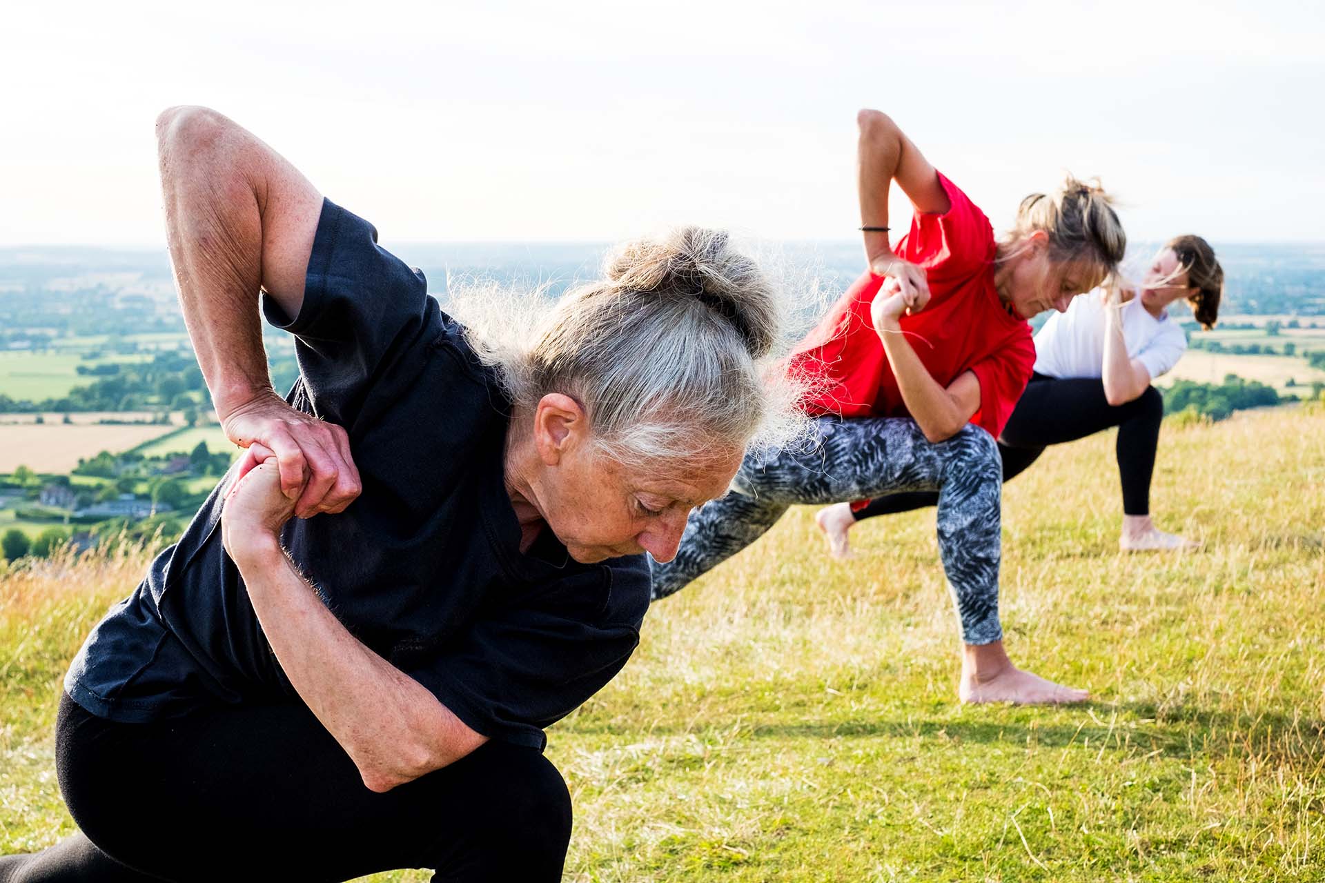 Group of women taking part in a yoga class on a hillside.